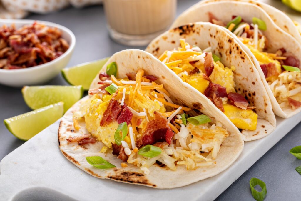 Breakfast tacos with scrambled eggs, bacon, and potato, topped with cheese